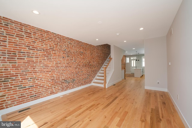 empty room featuring light wood finished floors, visible vents, recessed lighting, and brick wall