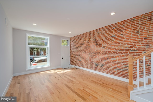 unfurnished room featuring brick wall, baseboards, stairway, recessed lighting, and wood finished floors