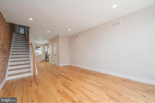 unfurnished living room with stairway, visible vents, brick wall, light wood finished floors, and recessed lighting