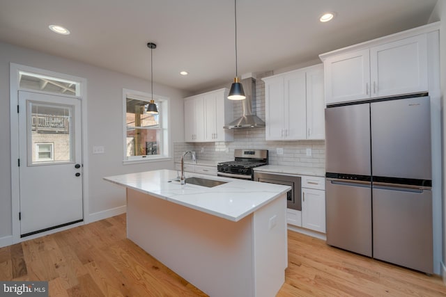 kitchen featuring light wood-style flooring, a sink, white cabinetry, stainless steel appliances, and wall chimney exhaust hood