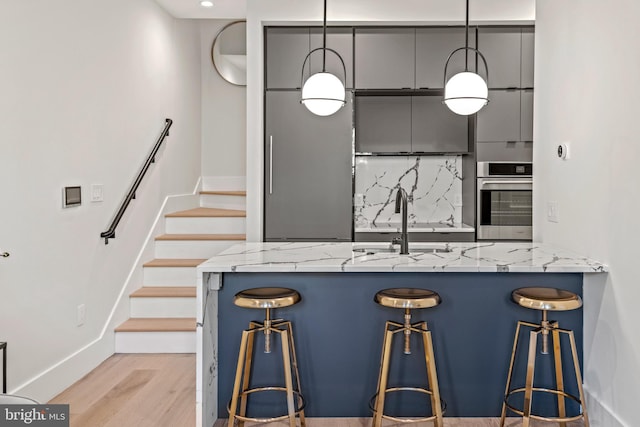 kitchen with oven, light stone counters, decorative backsplash, light wood-style floors, and a sink