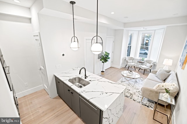 kitchen featuring baseboards, light wood-type flooring, light stone counters, a peninsula, and a sink