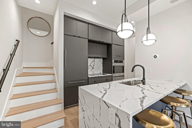 kitchen featuring gray cabinetry, a sink, a kitchen bar, stainless steel oven, and backsplash