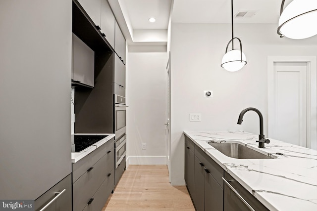 kitchen with light wood finished floors, visible vents, gray cabinetry, stainless steel oven, and a sink