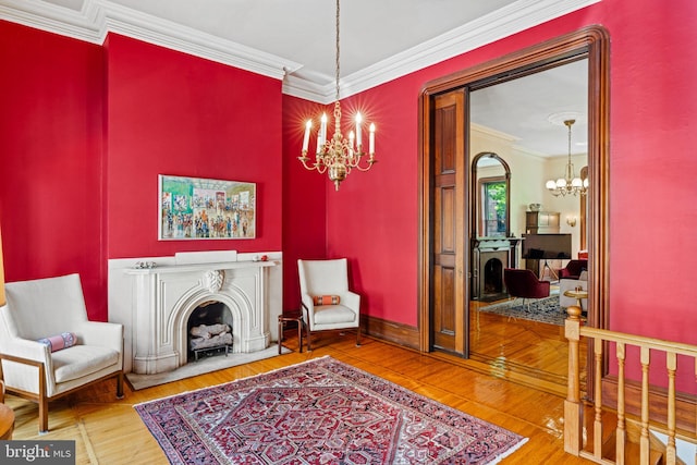 living area with baseboards, ornamental molding, a fireplace, an inviting chandelier, and wood finished floors