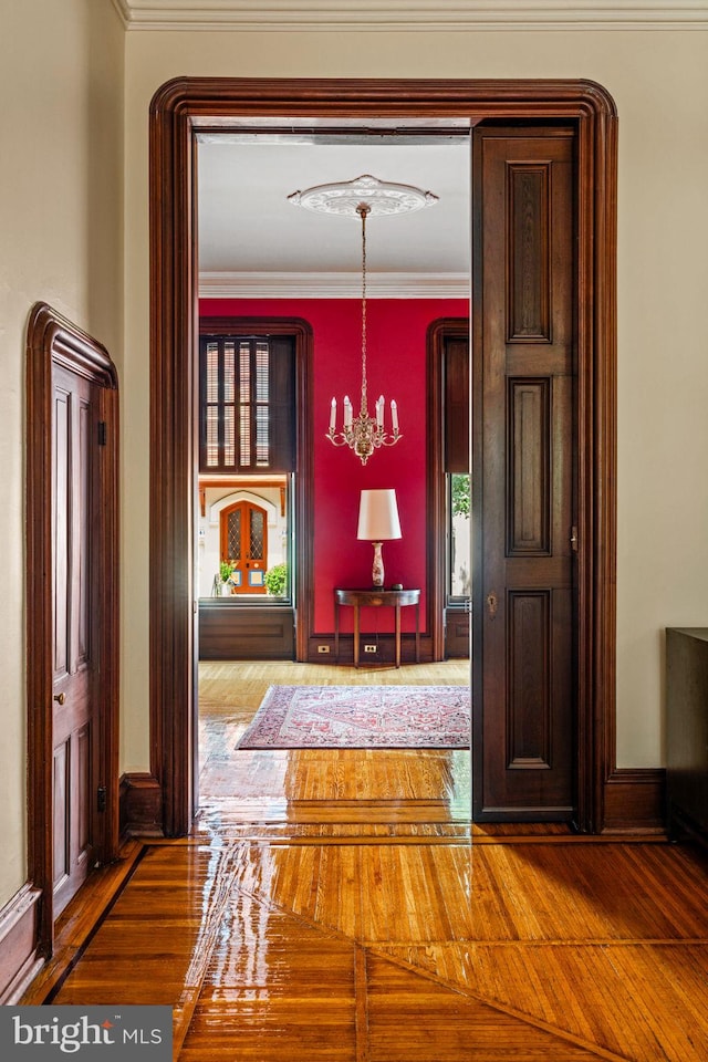 corridor with a healthy amount of sunlight, crown molding, an inviting chandelier, and wood finished floors