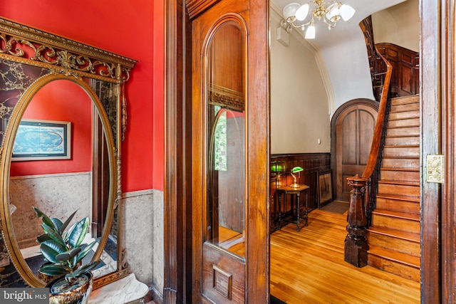 hallway with wood finished floors, arched walkways, stairs, wainscoting, and a chandelier