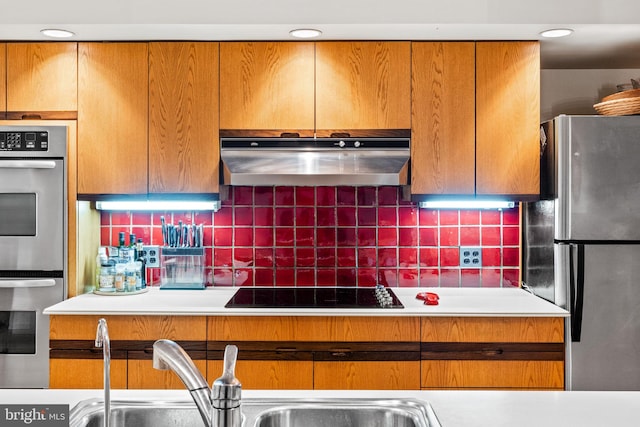 kitchen featuring a sink, decorative backsplash, light countertops, stainless steel appliances, and under cabinet range hood