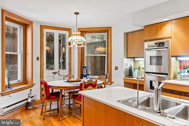 kitchen featuring baseboard heating, brown cabinets, light wood-style floors, stainless steel double oven, and a sink