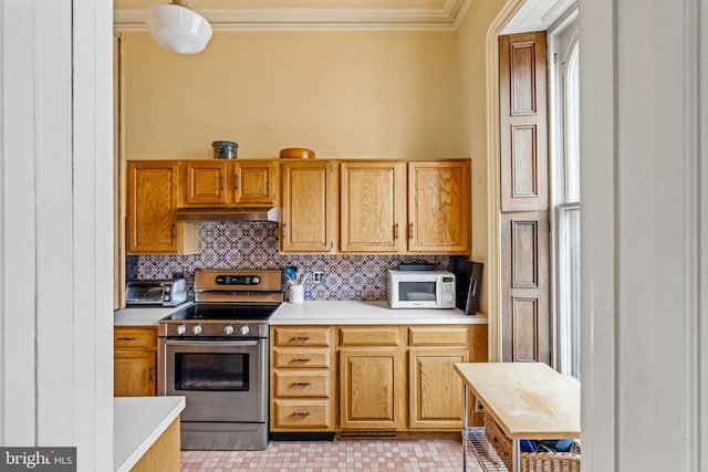 kitchen with white microwave, crown molding, under cabinet range hood, light countertops, and stainless steel range with electric cooktop