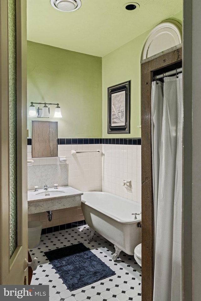 full bath featuring a wainscoted wall, a shower with curtain, toilet, tile walls, and a freestanding bath