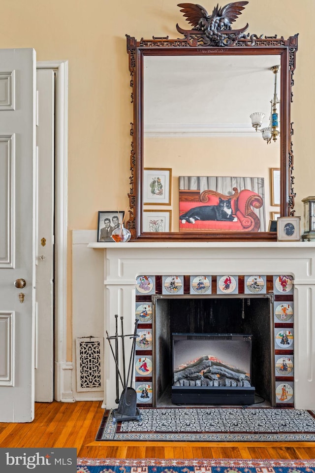 details with a tiled fireplace, a chandelier, and wood finished floors