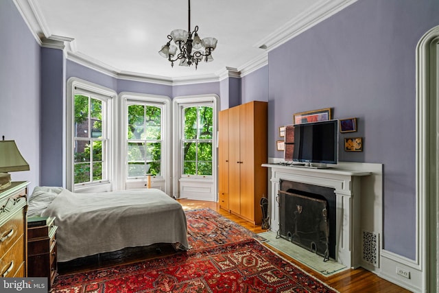 bedroom with a fireplace with flush hearth, an inviting chandelier, wood finished floors, and ornamental molding