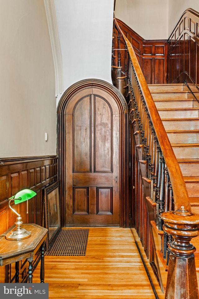 entrance foyer with light wood-type flooring, a decorative wall, wainscoting, and stairway