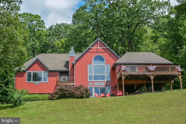 rear view of property featuring a deck, a lawn, roof with shingles, and a chimney