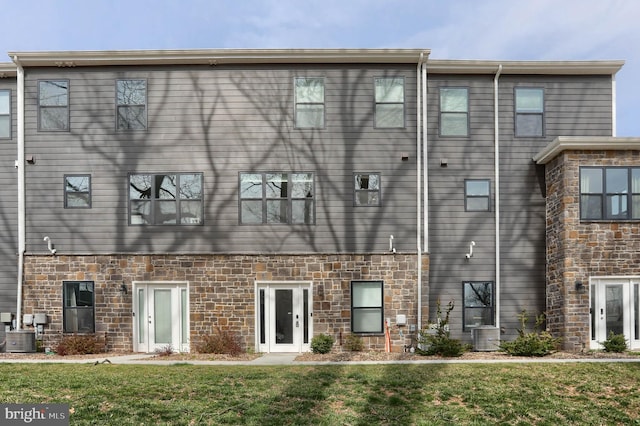 rear view of house featuring a yard, central AC unit, and stone siding