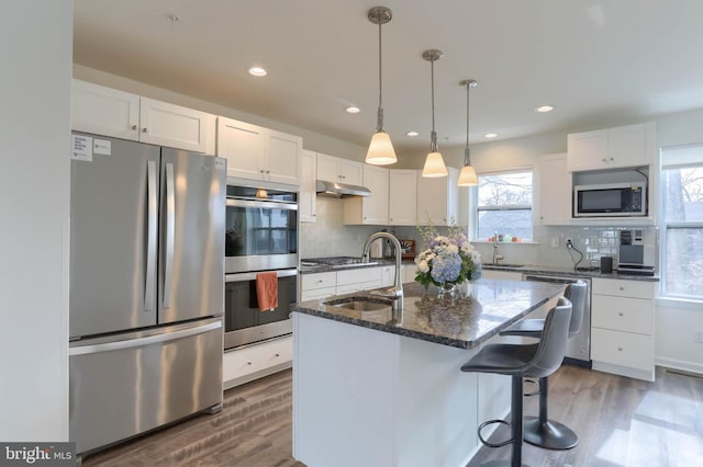 kitchen with wood finished floors, a sink, stainless steel appliances, white cabinets, and under cabinet range hood