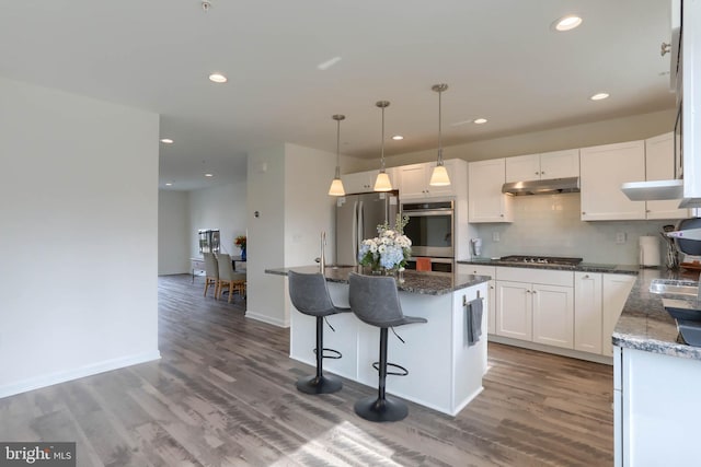 kitchen featuring tasteful backsplash, a center island, under cabinet range hood, stainless steel appliances, and white cabinetry