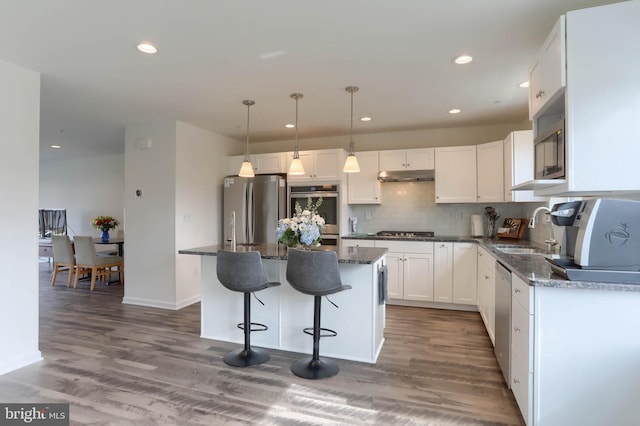 kitchen featuring a kitchen island, under cabinet range hood, appliances with stainless steel finishes, white cabinets, and a sink