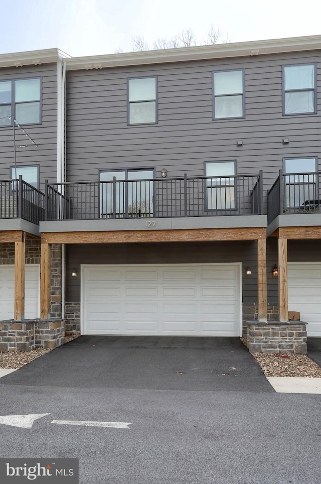 back of house featuring stone siding, an attached garage, and driveway