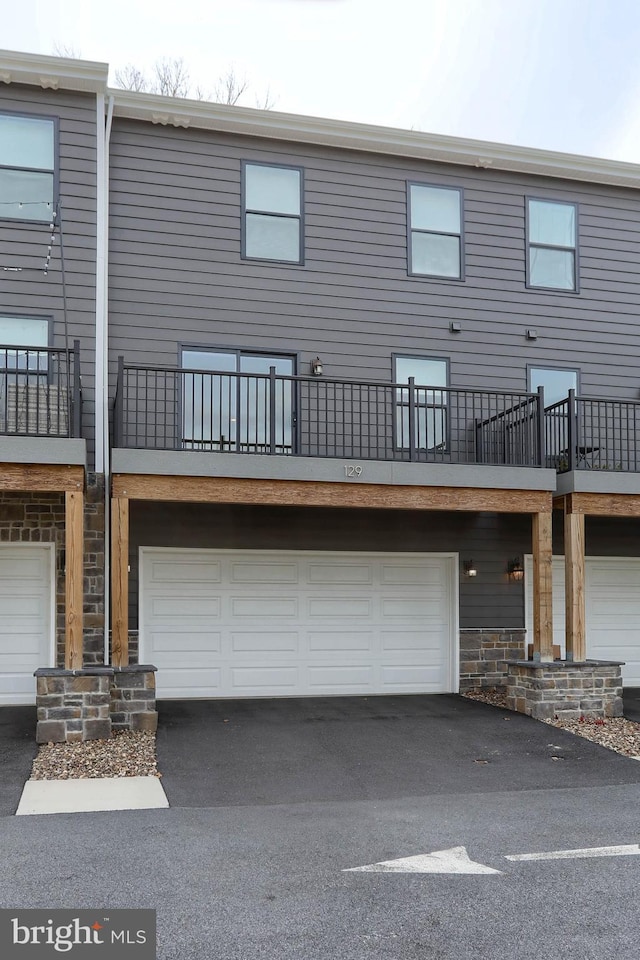 rear view of property with an attached garage, stone siding, and driveway