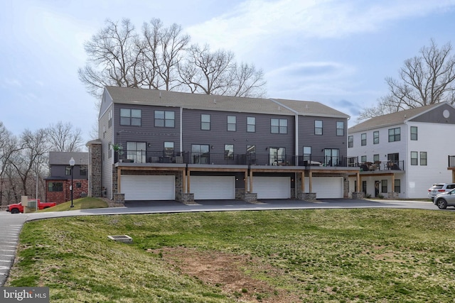 back of property featuring an attached garage, stone siding, driveway, and a yard