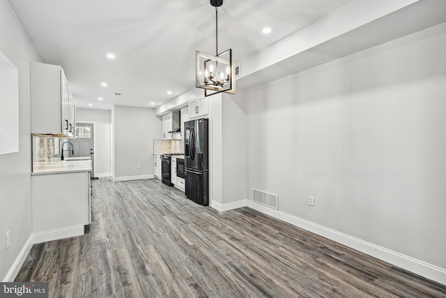 kitchen featuring visible vents, backsplash, light countertops, black appliances, and dark wood-style flooring