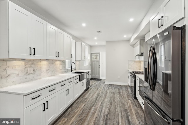 kitchen featuring a sink, black gas stove, white cabinetry, freestanding refrigerator, and dark wood-style flooring