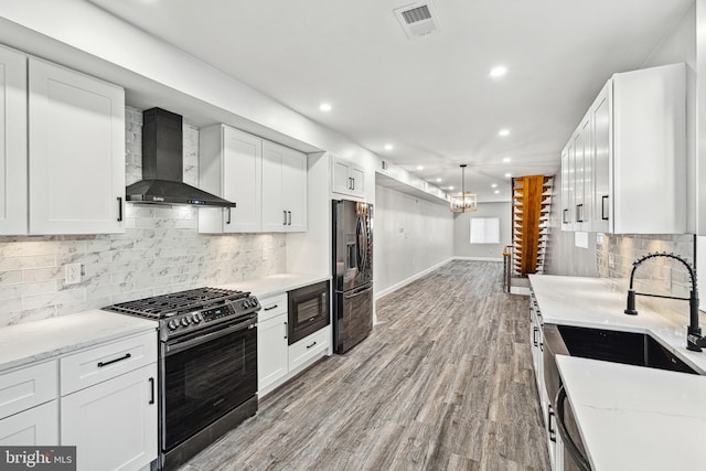 kitchen with visible vents, black appliances, wall chimney range hood, light wood-style flooring, and white cabinetry