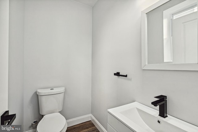 bathroom featuring baseboards, toilet, wood finished floors, and vanity