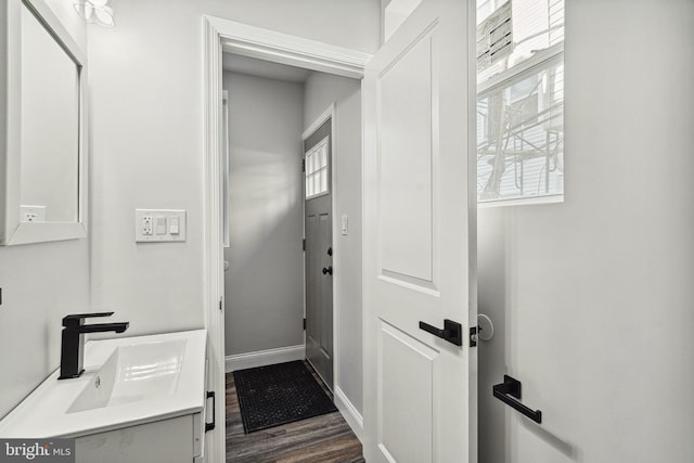 doorway to outside featuring a sink, baseboards, a healthy amount of sunlight, and dark wood-style flooring