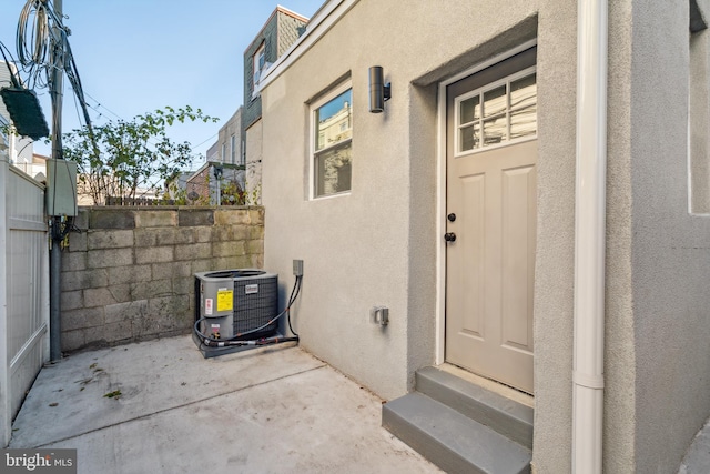 property entrance featuring central AC unit, fence, a patio, and stucco siding