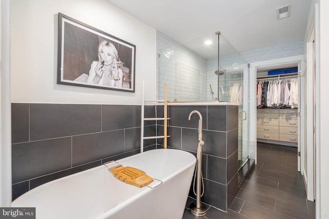 bathroom with visible vents, a walk in closet, a stall shower, a soaking tub, and tile walls