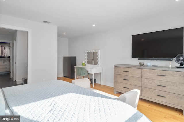 bedroom with a walk in closet, recessed lighting, wood finished floors, and visible vents