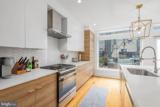 kitchen with stainless steel gas stove, a notable chandelier, modern cabinets, wall chimney exhaust hood, and light wood finished floors