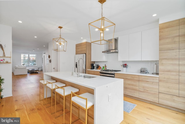 kitchen with modern cabinets, a sink, stainless steel appliances, light wood-style floors, and wall chimney exhaust hood