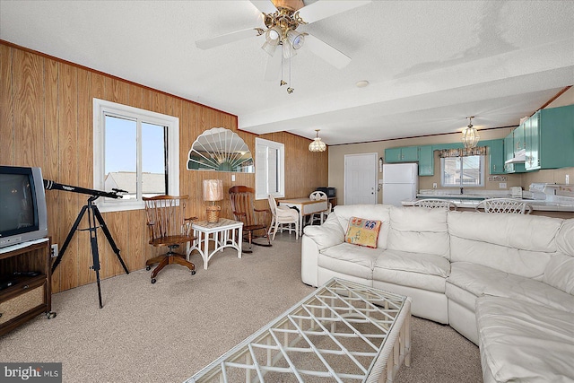 living area featuring a ceiling fan, light colored carpet, wooden walls, and a textured ceiling