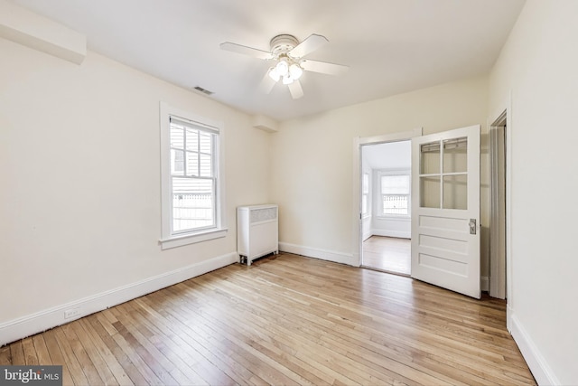 empty room with light wood finished floors, visible vents, radiator, baseboards, and a ceiling fan