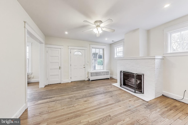 foyer entrance featuring a fireplace with flush hearth, wood finished floors, radiator heating unit, baseboards, and ceiling fan