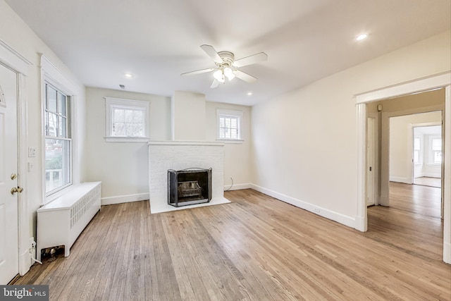 unfurnished living room with wood finished floors, radiator, baseboards, a brick fireplace, and ceiling fan