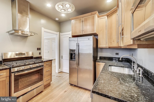 kitchen with light wood finished floors, a sink, light brown cabinetry, appliances with stainless steel finishes, and wall chimney range hood