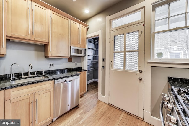 kitchen with light brown cabinets, dark stone countertops, light wood-style flooring, appliances with stainless steel finishes, and a sink