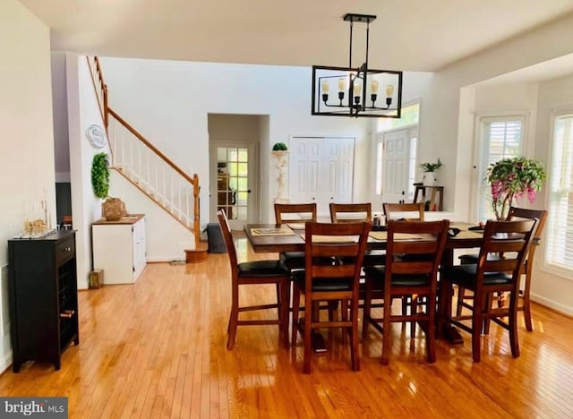 dining area featuring stairway, a notable chandelier, baseboards, and light wood-type flooring