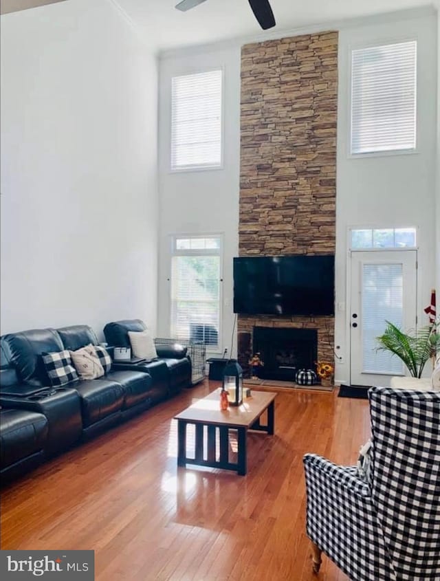 living room with a towering ceiling, a fireplace, wood finished floors, and a ceiling fan