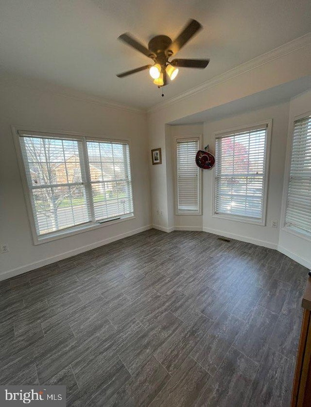 spare room with baseboards, dark wood-type flooring, ornamental molding, and a ceiling fan