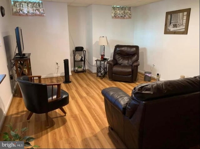 living area with baseboards, light wood-type flooring, and a drop ceiling