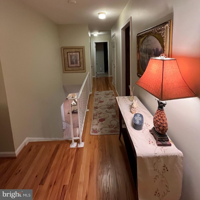 corridor with an upstairs landing, baseboards, and wood finished floors