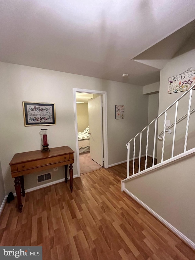 corridor with visible vents, stairway, baseboards, and wood finished floors