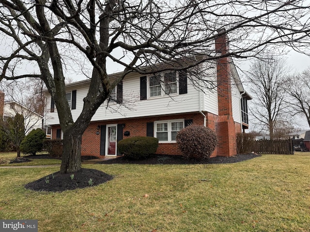 colonial home featuring brick siding, a chimney, and a front yard