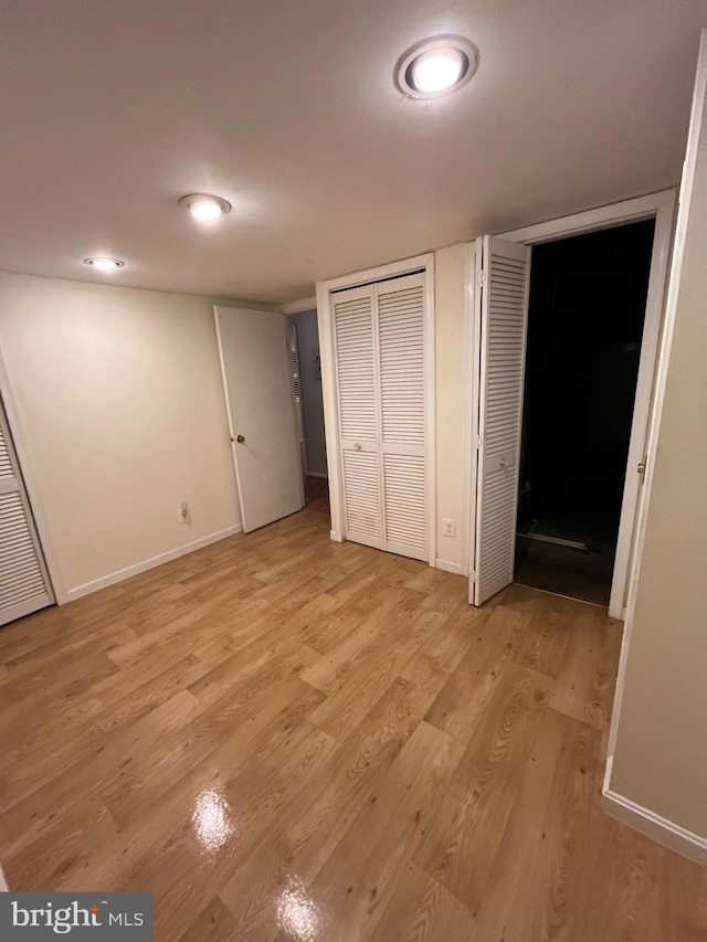 unfurnished bedroom featuring light wood finished floors, baseboards, and multiple closets